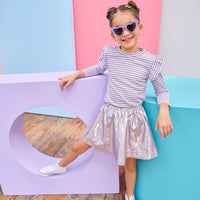 Child in a striped shirt and metallic skirt standing against colorful geometric shapes.