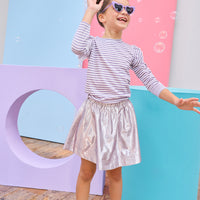 Young girl in a striped shirt and shiny skirt posing in front of colorful geometric shapes.