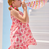 Model can be seen wearing a woven wide strap dress in a red/salmon pink floral print that features faux bow detail on strap and smocking across the bust for a secure but comfy fit.