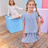 Two young girls in skorts with colorful blocks on a wooden floor.