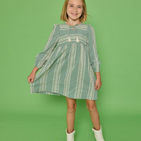 Model can be seen wearing a long sleeve woven seersucker dress in a green and cream pattern. Dress features tie with tassels at v-neckline for an elevated look.