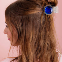 Woman with a hair bun featuring a decorative hair clip with a blue gem on a pink background