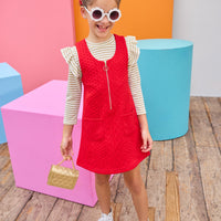 Young girl in a red dress with a gold striped top underneath with colorful geometric shapes in the background