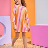 Young girl wearing a colorful striped dress in front of geometrically colored blocks.