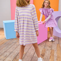 Two young girls in purple dresses standing in a room with a wooden floor and colorful walls.