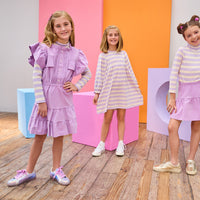Three young girls in colorful dresses standing in a room with colorful blocks.