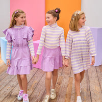 Three young girls holding hands in front of colorful geometric shapes wearing matching outfits.
