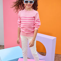 Tween model seen wearing a striped light pink and hot pink sweater paired back with ivory jeans for a comfy yet elevated look.