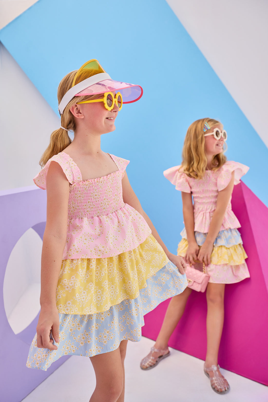 Model in the front can be seen wearing woven tiered dress that features a stretchy ruching detail across bust and three tiers of a combination of pink/yellow/and blue floral patterns. Dress also features angel sleeve detail at straps for the finishing touch. Model in back can be seen wearing same floral print in our India top and tiered skort for a matching outfit moment.