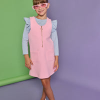 Model can be seen wearing a blue and white stripe long sleeve knit top with ruffles at the sleeves paired under a bubblegum pink quilted jumper. Jumper features quarter zip zipper down front and pockets.