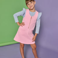 Model can be seen wearing a blue and white stripe long sleeve knit top with ruffles at the sleeves paired under a bubblegum pink quilted jumper. Jumper features quarter zip zipper down front and pockets.