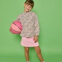 Model can be seen wearing a woven top with a ruffle neckline and button closure along back. The brown/pink/blue floral print pairs back perfectly with our quilted knit mini skirt in bubblegum pink to complete the look.