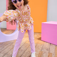 Child wearing a floral top and purple pants with colorful background