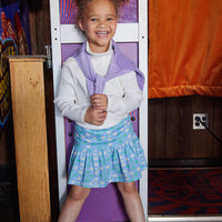 Model can be seen wearing our Sadie Skort in Seville Azul paired with our Ribbed Turtleneck in Ivory, which is layered under our Lilac Polo Pullover to complete the look--BISBY girl
