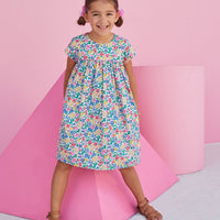 Girl wearing BISBY floral dress with pink piping and a colorful floral print.