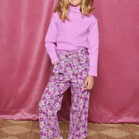 Tween woven pant with pockets in a purple/magenta/pink floral pattern that comes with a belt in the matching print and button/zipper closure in front of pants paired back with a magenta ribbed turtleneck.