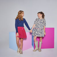 Model on the left can be seen wearing a ribbed turtleneck in our navy color made of a super soft/stretchy/thick material paired back with a circle skirt in a cranberry color. Model on the right can be seen wearing a matching outfit in our Madaket dress in navy which features a v-neckline and hot pink ric rac detail across middle.