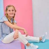 BISBY girl with braided hair sitting on a colorful platform wearing white jeans and a blue crinkle top with silver stars.