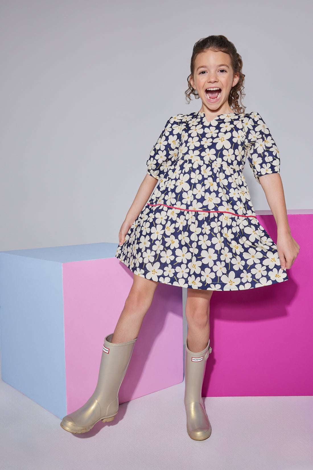 Girls/tween woven dress with  elbow length slight puff sleeves, slight v-neck keyhole neckline in a navy/white floral pattern with a hot pink trim  piping along bottom tier of dress.