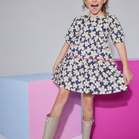 Girls/tween woven dress with elbow length slight puff sleeves, slight v-neck keyhole neckline in a navy/white floral pattern with a hot pink trim piping along bottom tier of dress.