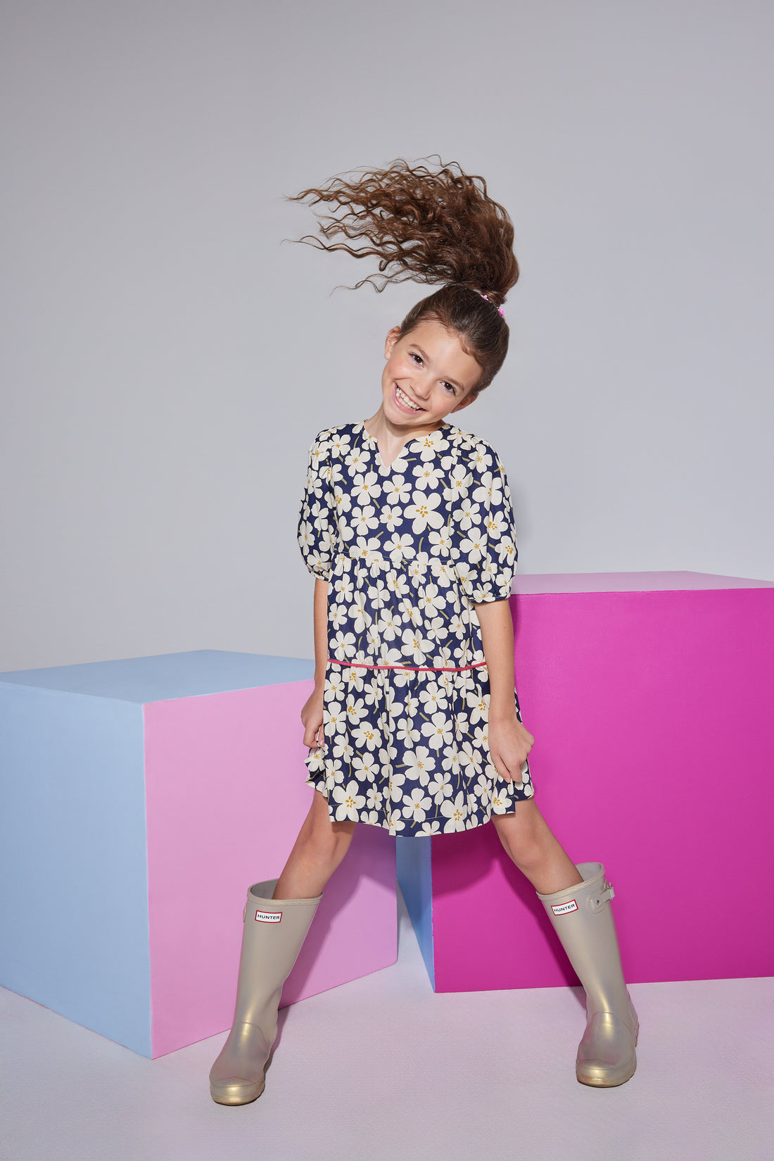 Girls/tween woven dress with elbow length slight puff sleeves, slight v-neck keyhole neckline in a navy/white floral pattern with a hot pink trim piping along bottom tier of dress.