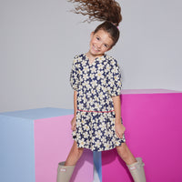 Girls/tween woven dress with elbow length slight puff sleeves, slight v-neck keyhole neckline in a navy/white floral pattern with a hot pink trim piping along bottom tier of dress.