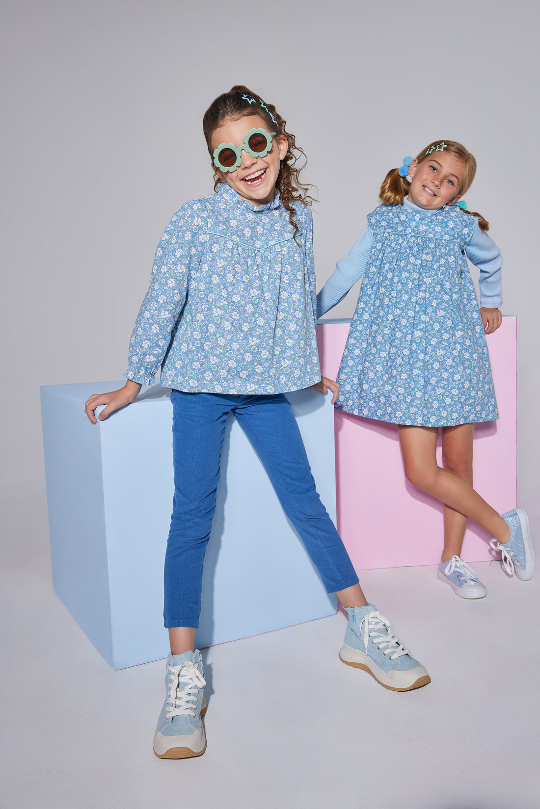 Model on left can be seen wearing corduroy pants in a deep blue color. Pants are made of a soft corduroy material and feature a button/snap closure at zipper for easy put on access. Pants can be seen paired back with a long sleeve woven top in a blue floral pattern to complete the look.Model on right can be seen wearing a dress in the matching blue floral pattern with an ice blue ribbed turtleneck underneath to complete the matching looks.