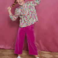 Girls/tween woven long sleeve top in a magenta/pink/orange/green floral pattern which features a ruffle neckline, elastic cuffs at end of sleeves, and slight gathering across bust for a relaxed comfy fit. These tops pair back greatly with our velour pants in the magenta color to complete the look.