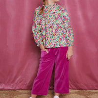 Tween girl cropped magenta velour pants which have pockets in the front and an elastic waistband. Can be seen paired with a long sleeve woven shirt with a ruffle neckline in a magenta/pink/orange/green floral print.