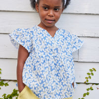 blue floral top for little girls and tweens. v-neck top with white scallop trim along sleeves and bottom of the top. Has a light blue background with white flowers