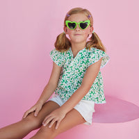 BISBY girl in our Positano Blouse in Piccadilly Lawn. A beautiful green base with white and yellow floral pattern. Shirt has scalloped edges on the sleeves and bottom of shirt and has a v-neck making it easy to get in and out of