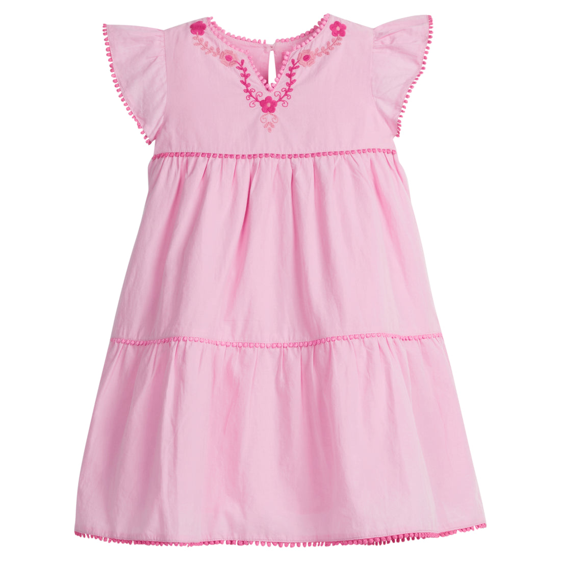 Girls/Tween woven pink tiered dress with hot pink and light pink embroidery detail on chest/along the v-neck neckline. Dress also features hot pink pom poms along sleeve and first and bottom tiers of dress. A row of light pink pom poms is seen along the second tier of dress and around neckline. There is also a button closure at back of neckline for a secure fit.