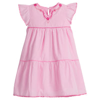 Girls/Tween woven pink tiered dress with hot pink and light pink embroidery detail on chest/along the v-neck neckline. Dress also features hot pink pom poms along sleeve and first and bottom tiers of dress. A row of light pink pom poms is seen along the second tier of dress and around neckline. There is also a button closure at back of neckline for a secure fit.