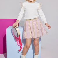 Girls/Tween skort in out Pink Metallic Stars and Stripes pattern. Skort is made of a woven light pink base fabric with a tulle overlay that has gold stars all over. Skort also has built in shorts and an elastic waistband in a gold glitter material. Pair back perfectly with our ivory knit long sleeve top with the same tulle fabric as angel sleeves to complete the look.