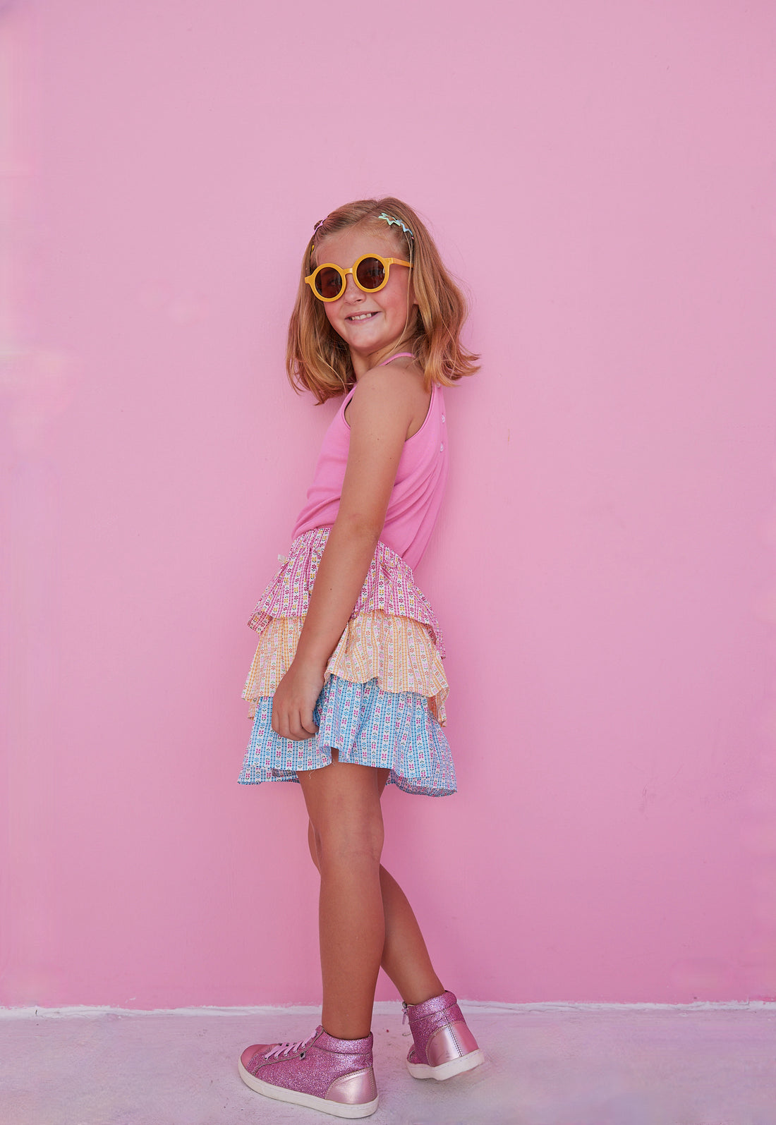 BISBY girl in our Tiered Mini Skort in our "Daisy Chain" with top tier in pink, middle tier in orange, and bottom tier in blue floral pattern. Skort has built in shorts and has elastic waistband. Paired perfectly with our Hot pink halter top