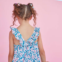 Our model is seen from behind wearing our Tribeca Dress in the print Green Hills Garden, which features ruffled V straps and light pink flowers with blue leaves