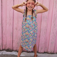Little girl wearing ruffle adjustable strap sundress which features a square neckline and a colorful floral print.