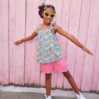 Little girl wearing ruffle adjustable strap top which features a square neckline and a colorful floral print.