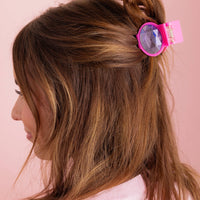 Person with a pink hair clip in their hair against a pink background