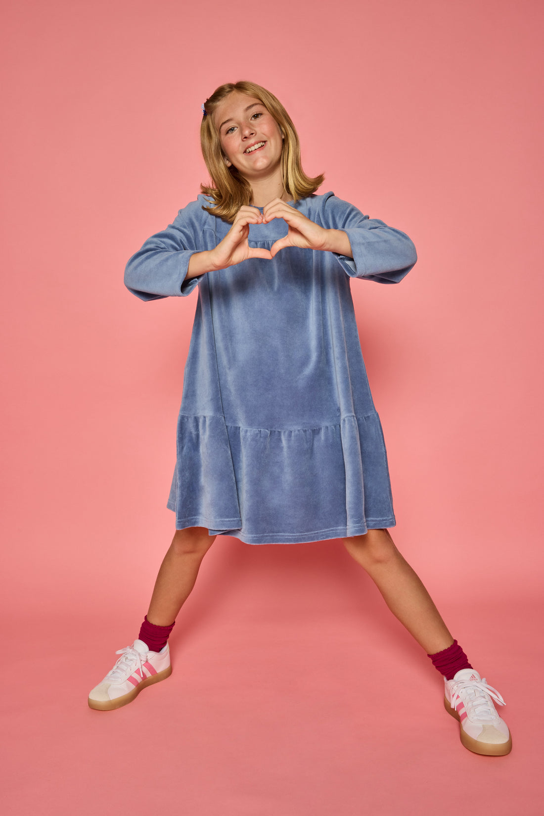 Model can be seen wearing a long sleeve dusty blue velour dress. Dress features button closure at back for a relaxed but secure fit. 