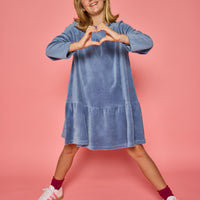 Model can be seen wearing a long sleeve dusty blue velour dress. Dress features button closure at back for a relaxed but secure fit. 