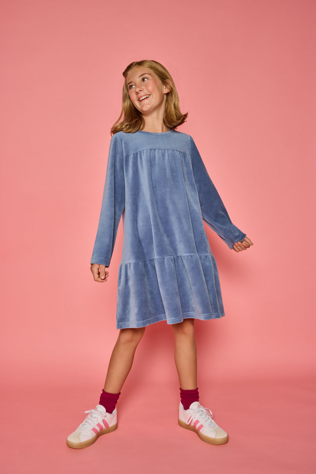 Model can be seen wearing a long sleeve dusty blue velour dress. Dress features button closure at back for a relaxed but secure fit. 