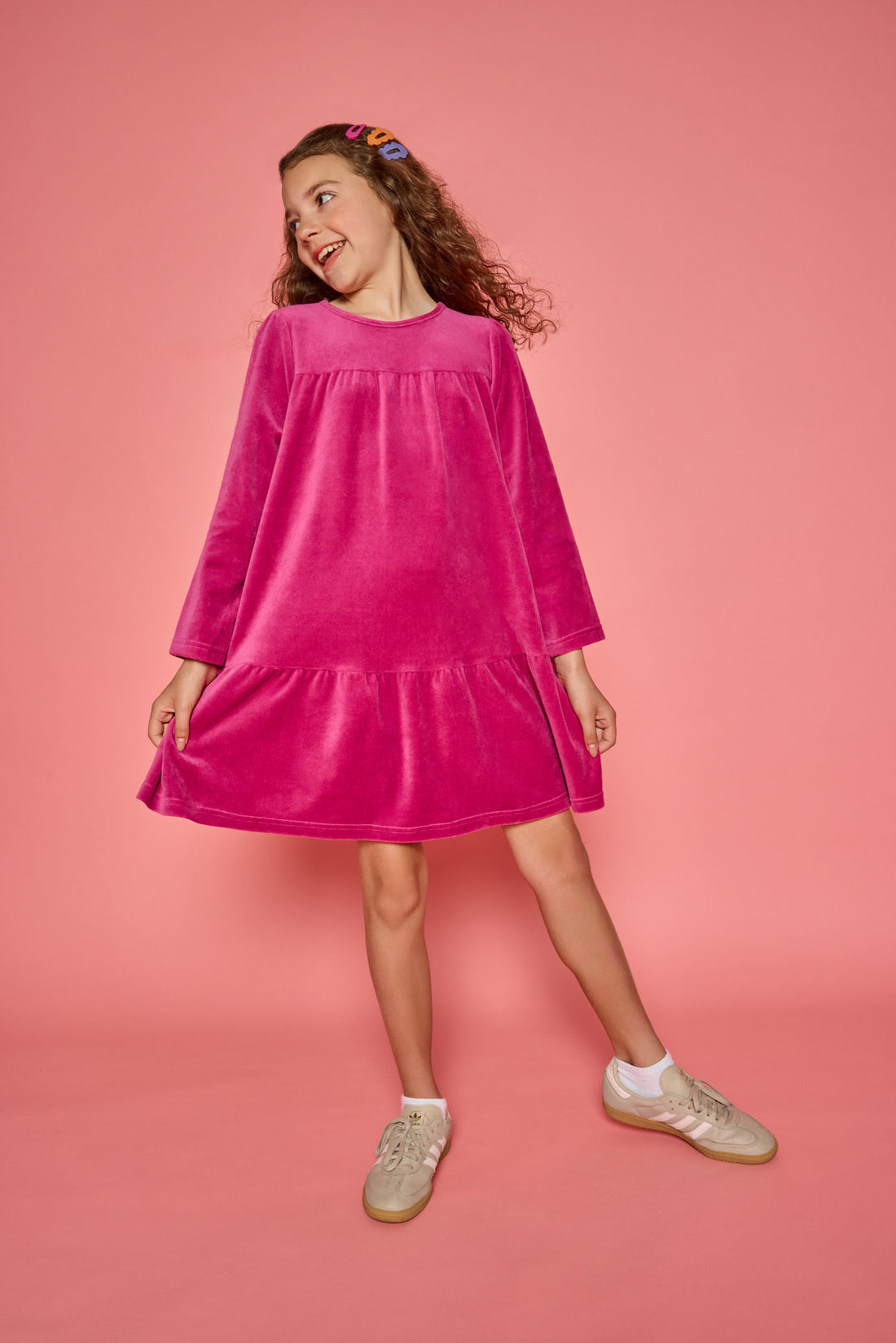 Model can be seen wearing a long sleeve magenta velour dress. Dress features button closure at back for a relaxed but secure fit. 