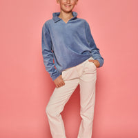 Model can be seen wearing a dusty blue velour pullover that features a fold over collar for easy over the head access. Paired back with basic white denim jeans to complete the look. 