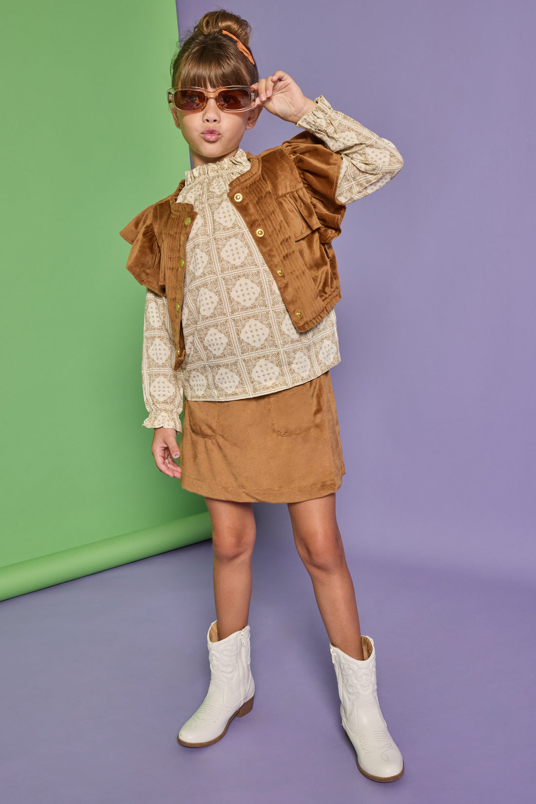 Model can be seen wearing a woven top in a tan/cream pattern that features ruffle detail at the neckline. Paired back underneath the faux brown suede top with angel sleeves and buttons down the front that pairs back with the matching brown faux suede skort to complete the look. 