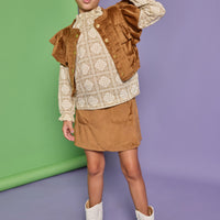 Model can be seen wearing a woven top in a tan/cream pattern that features ruffle detail at the neckline. Paired back underneath the faux brown suede top with angel sleeves and buttons down the front that pairs back with the matching brown faux suede skort to complete the look. 