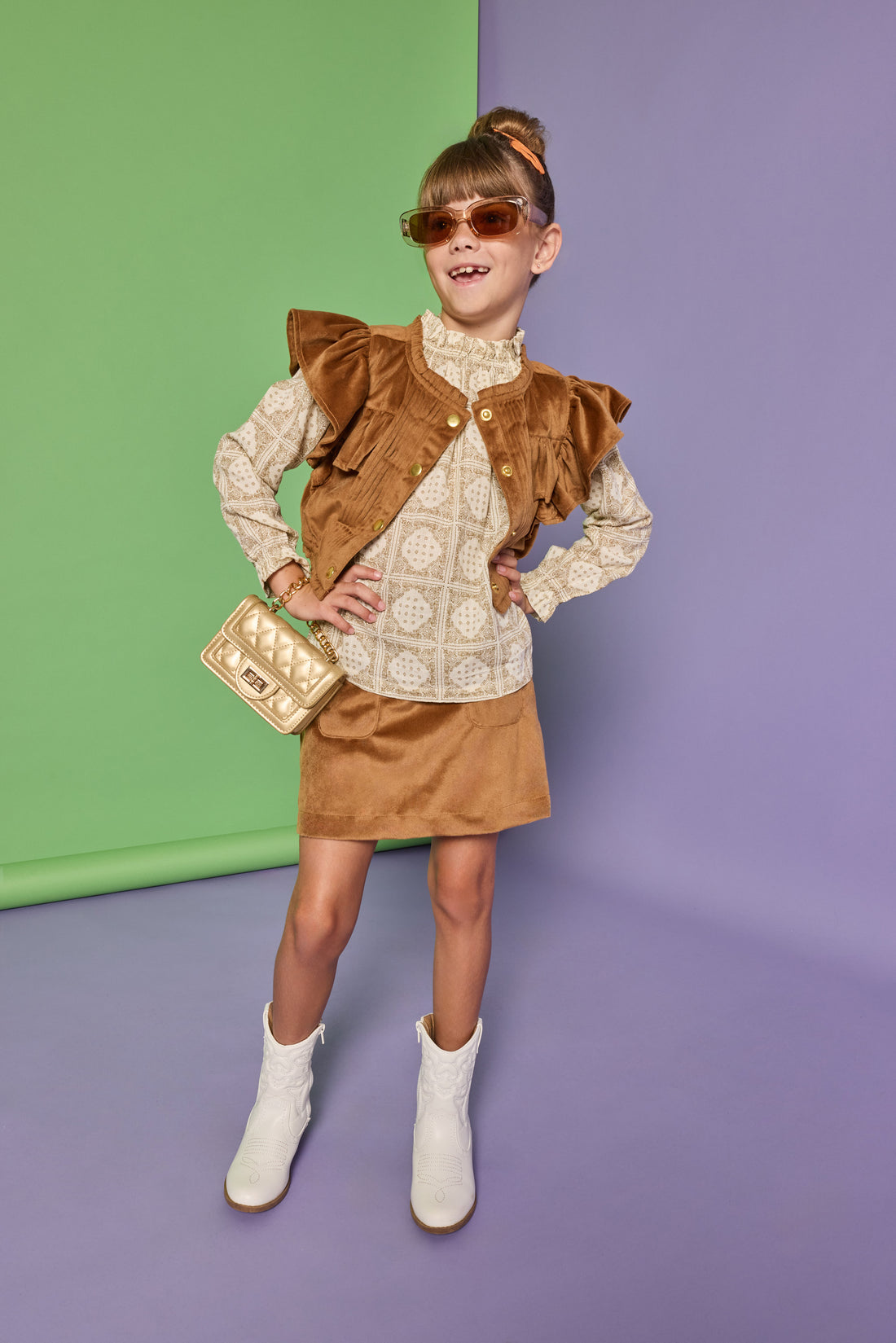 Model can be seen wearing a woven top in a tan/cream pattern that features ruffle detail at the neckline. Paired back underneath the faux brown suede top with angel sleeves and buttons down the front that pairs back with the matching brown faux suede skort to complete the look. 