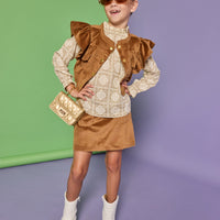 Model can be seen wearing a woven top in a tan/cream pattern that features ruffle detail at the neckline. Paired back underneath the faux brown suede top with angel sleeves and buttons down the front that pairs back with the matching brown faux suede skort to complete the look. 