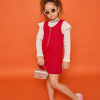 Model can be seen wearing white long sleeve ribbed knit top with ruffles at sleeves paired underneath cherry red sparkly knit jumper. Jumper features a quarter zip zipper and also features pockets at the front. 