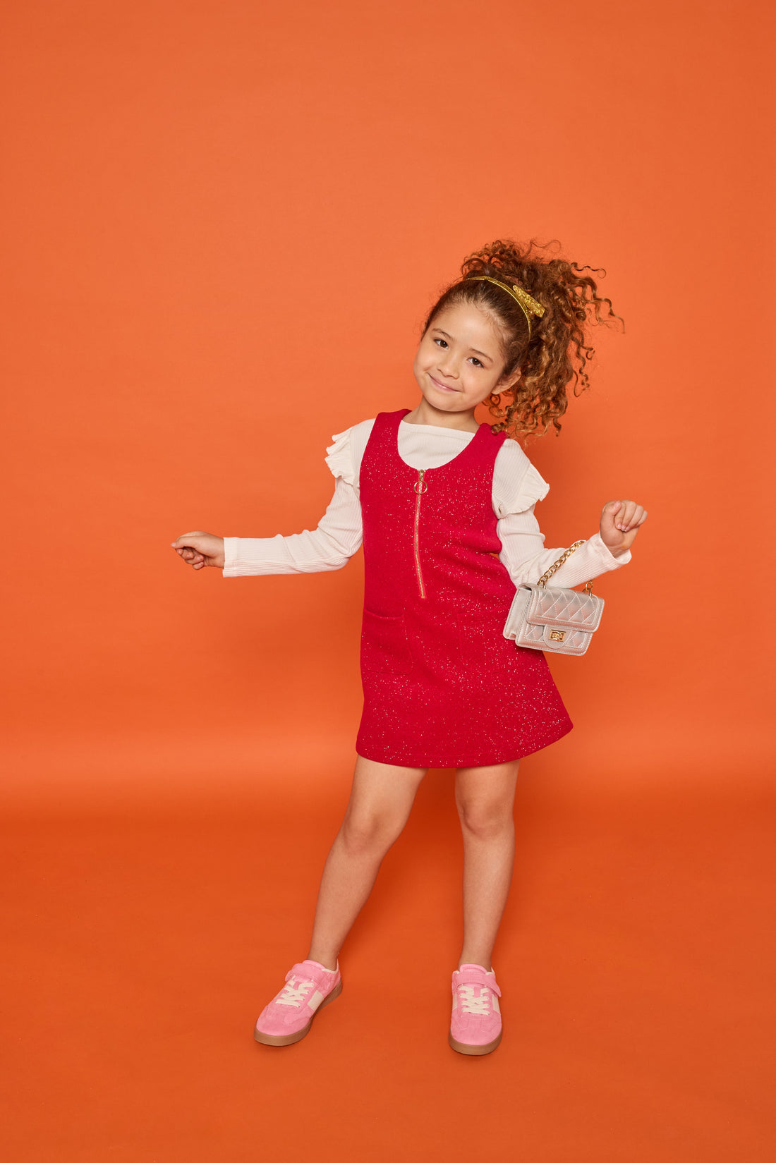 Model can be seen wearing white long sleeve ribbed knit top with ruffles at sleeves paired underneath cherry red sparkly knit jumper. Jumper features a quarter zip zipper and also features pockets at the front. 